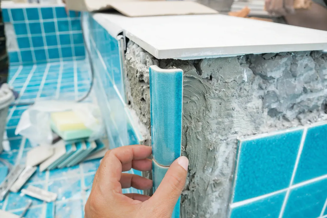 Close-up of new blue tile being placed on a pool edge with mortar